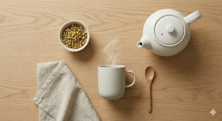 White teapot, mug of chamomile tea, and dried chamomile flowers on a wooden table.