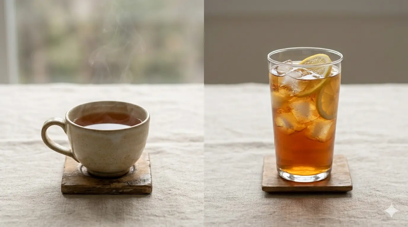 A cup of hot tea with steam rising from the sides, next to a glass of iced tea with lemon and ice, on a light-colored table.